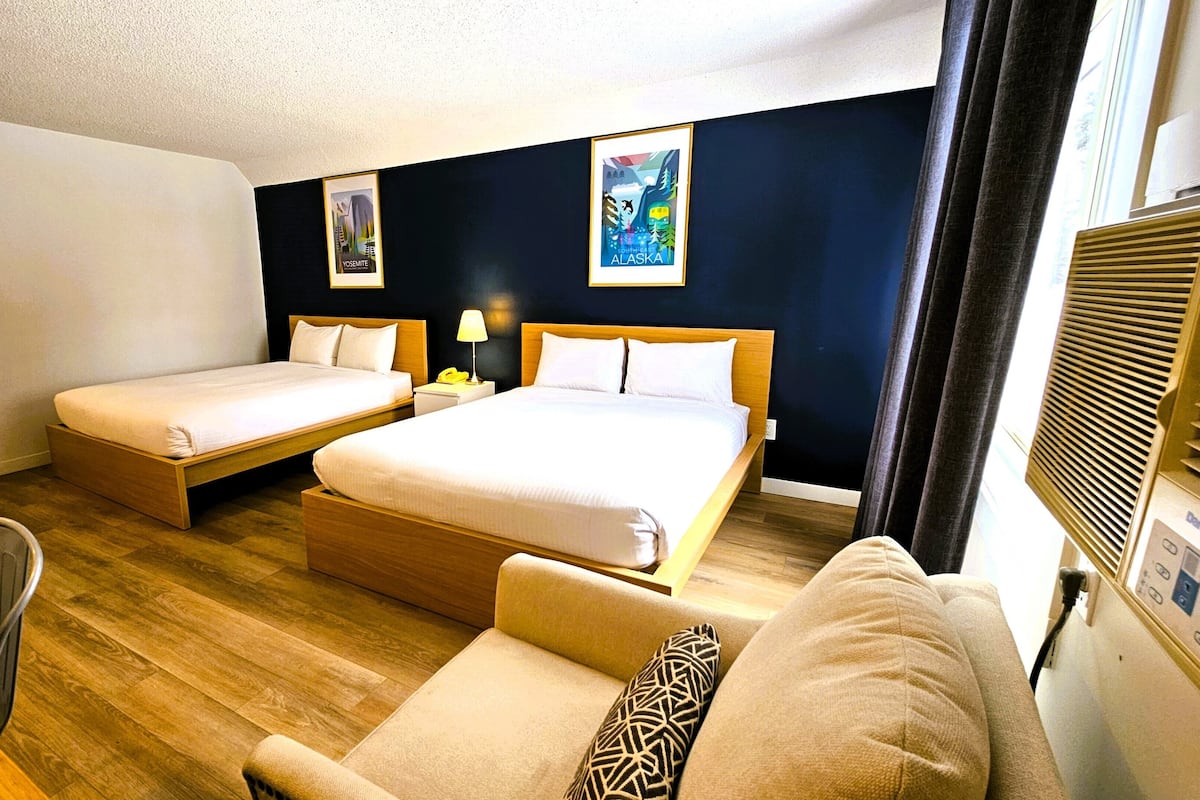 A hotel room with two single beds, a double bed, a wooden desk, a chair, and a couch.