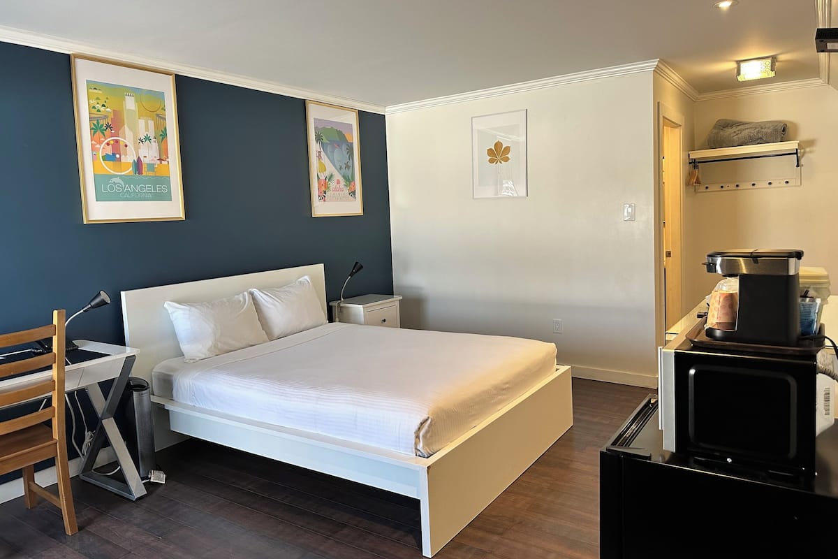 A bedroom with a bed, bedside tables, a desk, a chair, and a microwave.