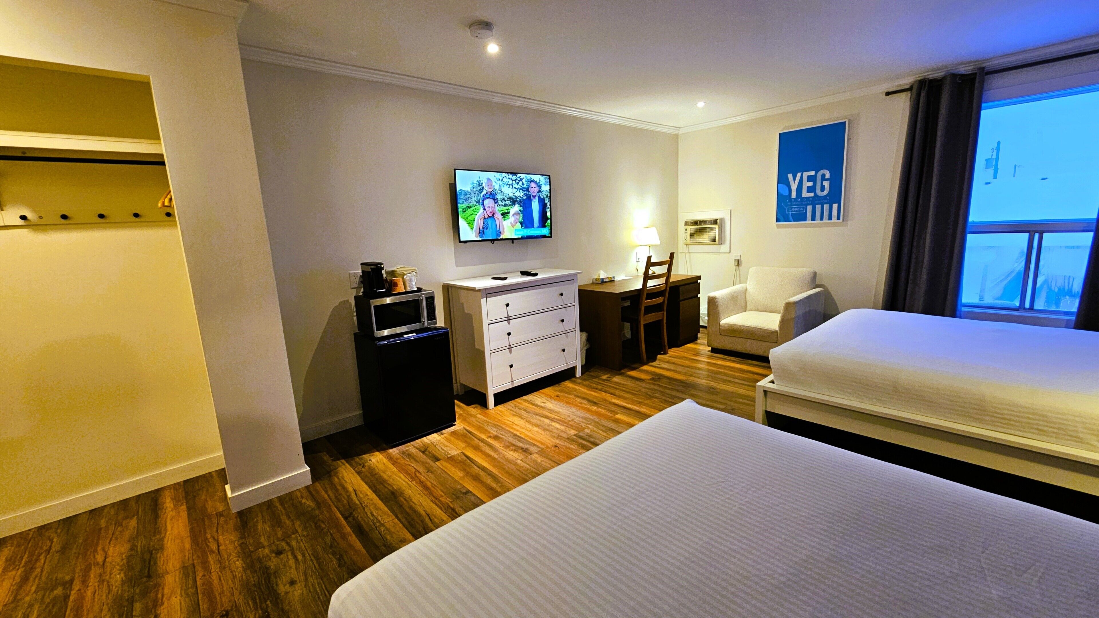 A hotel room with two beds, a TV, a desk, a chair, a dresser, and a window with a view.