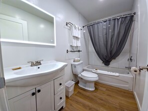 A bathroom with a white sink, toilet, and bathtub. There is a mirror above the sink and a shower curtain over the bathtub.