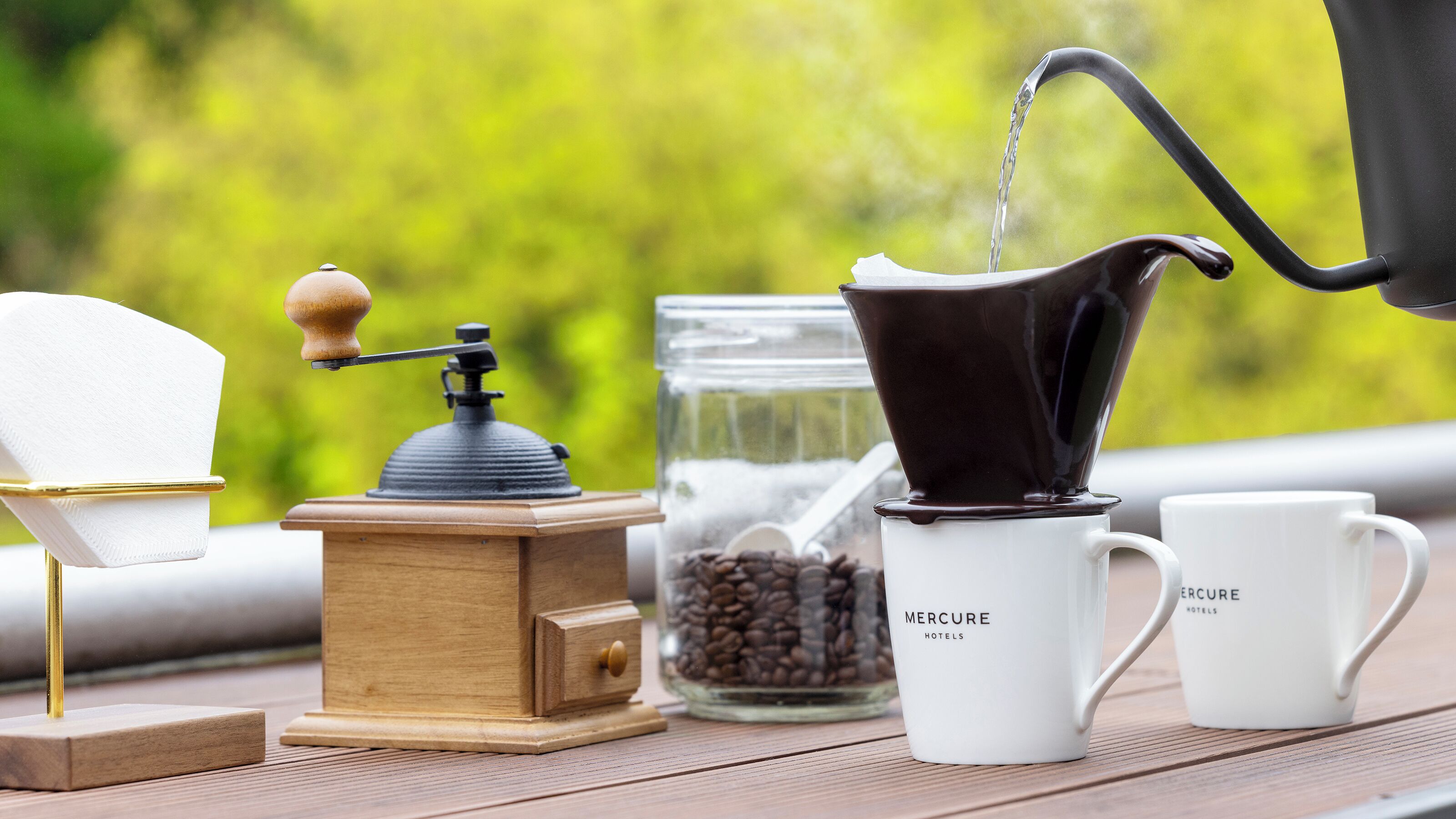Een koffiezetapparaat met een handmatige koffiemolen, een koffiekan en twee kopjes op een houten tafel.