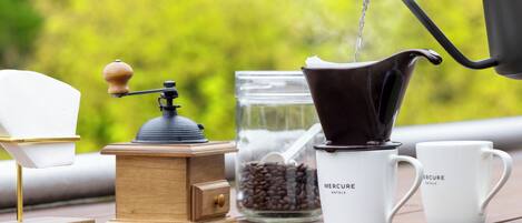 Een koffiezetapparaat met een handmatige koffiemolen, een koffiekan en twee kopjes op een houten tafel.