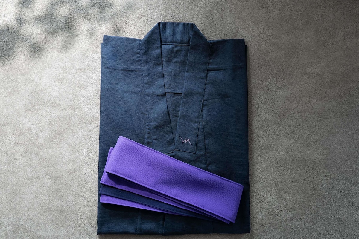 A folded dark blue shirt with a small white logo on the pocket, placed on a textured surface.