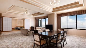 Une chambre d’hôtel spacieuse dotée d’une grande table à manger, de sièges confortables, d’un téléviseur à écran plat et de grandes fenêtres offrant une vue sur la ville.