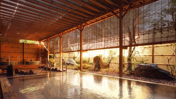 Un onsen japonais traditionnel doté d’une terrasse en bois, d’un bain en pierre et d’une clôture en bambou.
