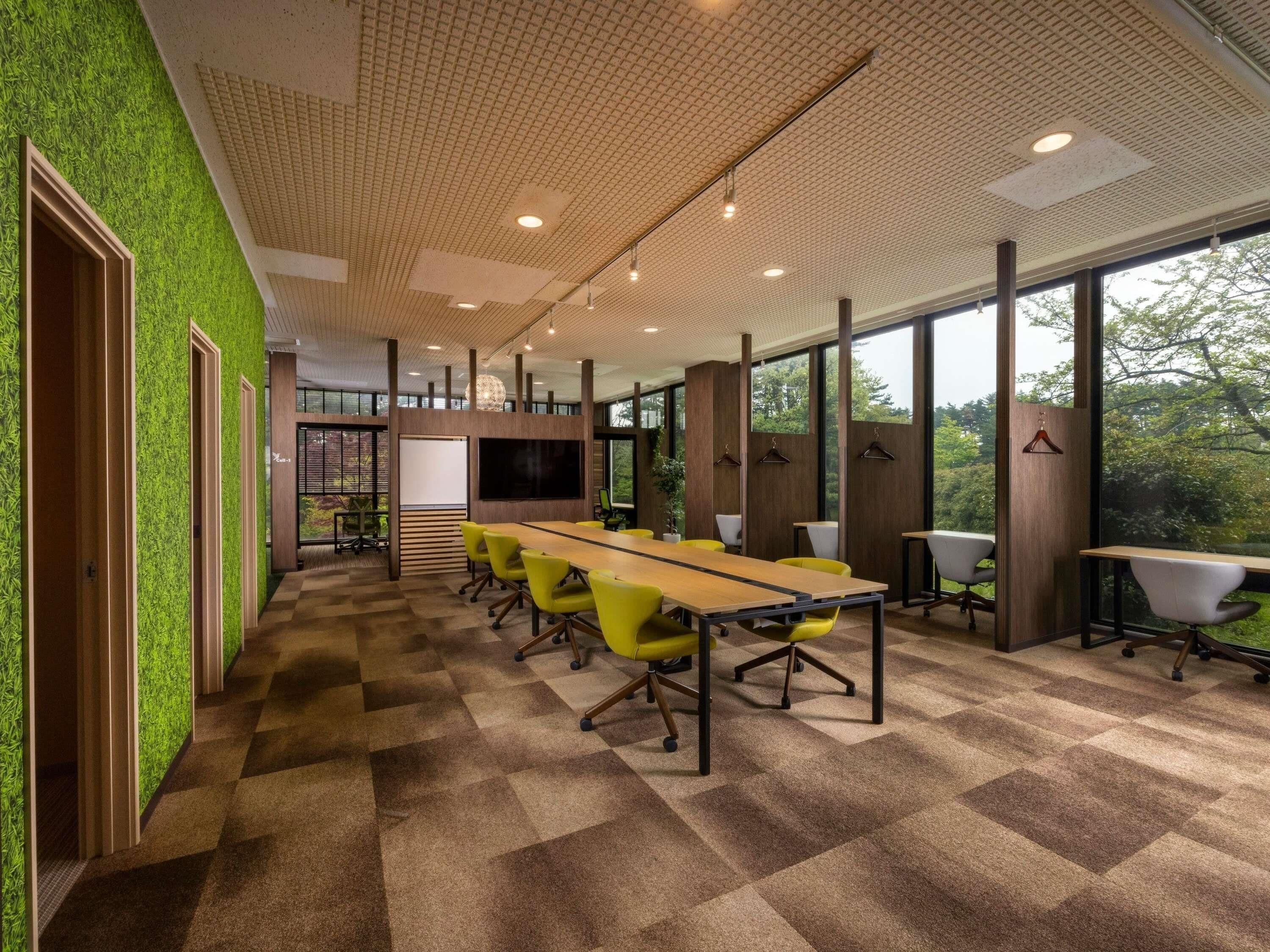 A conference room with a long table, chairs, a projector screen, and a large window with a view of trees.
