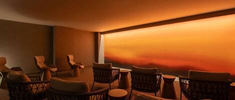 A dimly lit room with wicker chairs and a large window overlooking a sunset.