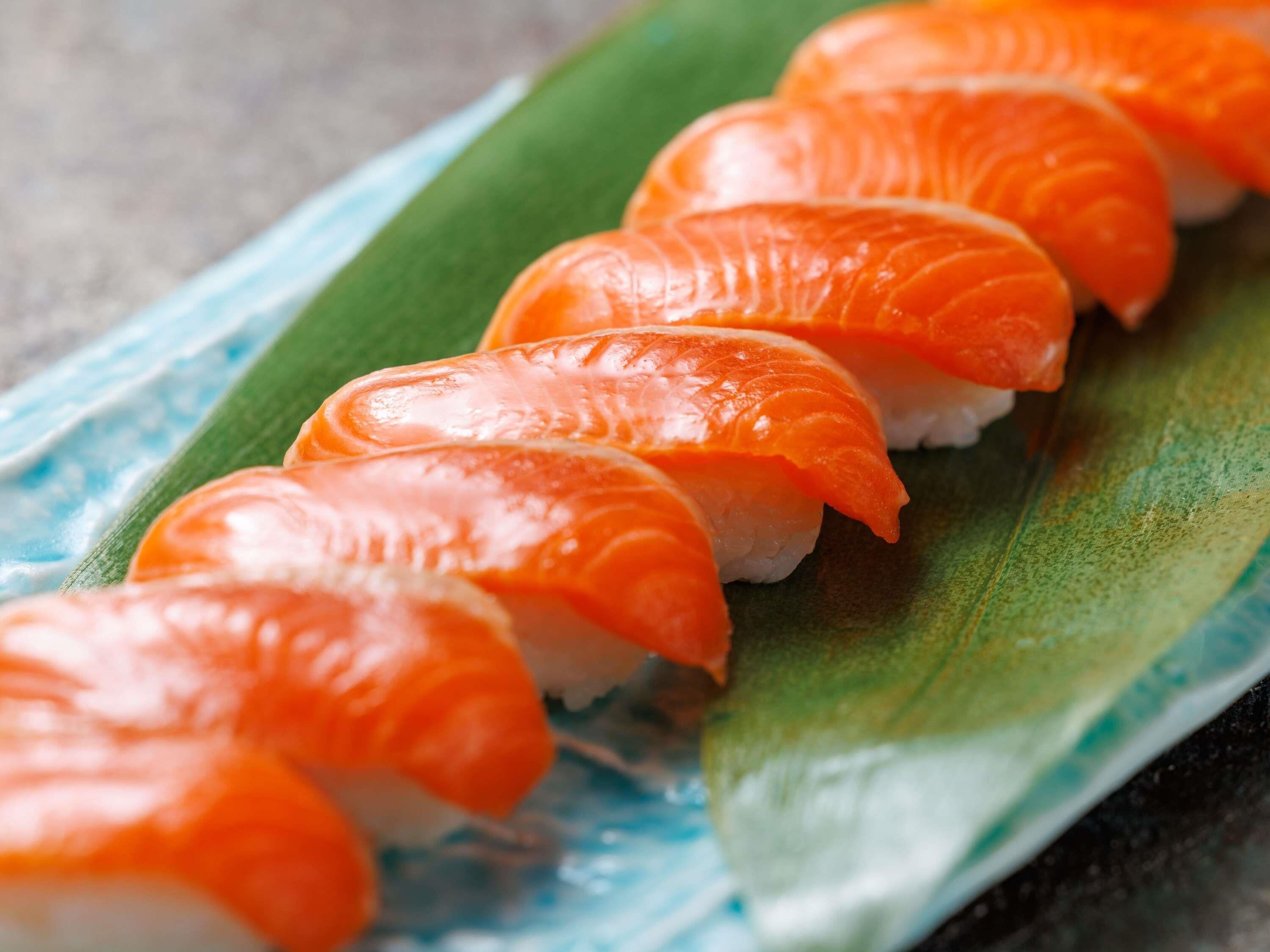 A plate of sushi with salmon slices on top of rice, placed on a green leaf.