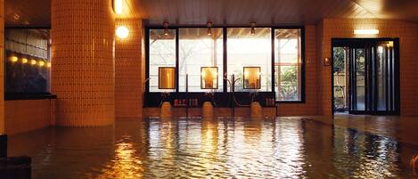 A spacious indoor area with a wooden floor and walls, large windows with framed pictures, and a door with glass panels.