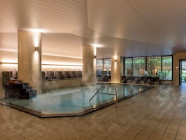 A modern indoor swimming pool with seating and a sauna area.