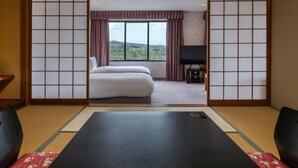 Une pièce de style japonais traditionnel, avec un sol recouvert de tatamis, un lit, une télévision et une vue sur un paysage boisé.