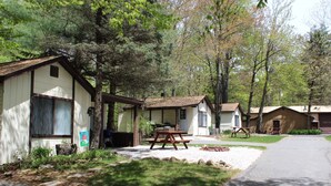 Una hilera de cabañas con mesas de picnic al frente, rodeadas de árboles.