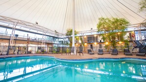 Una piscina interior con zona techada, sillas de descanso y vista del edificio circundante.