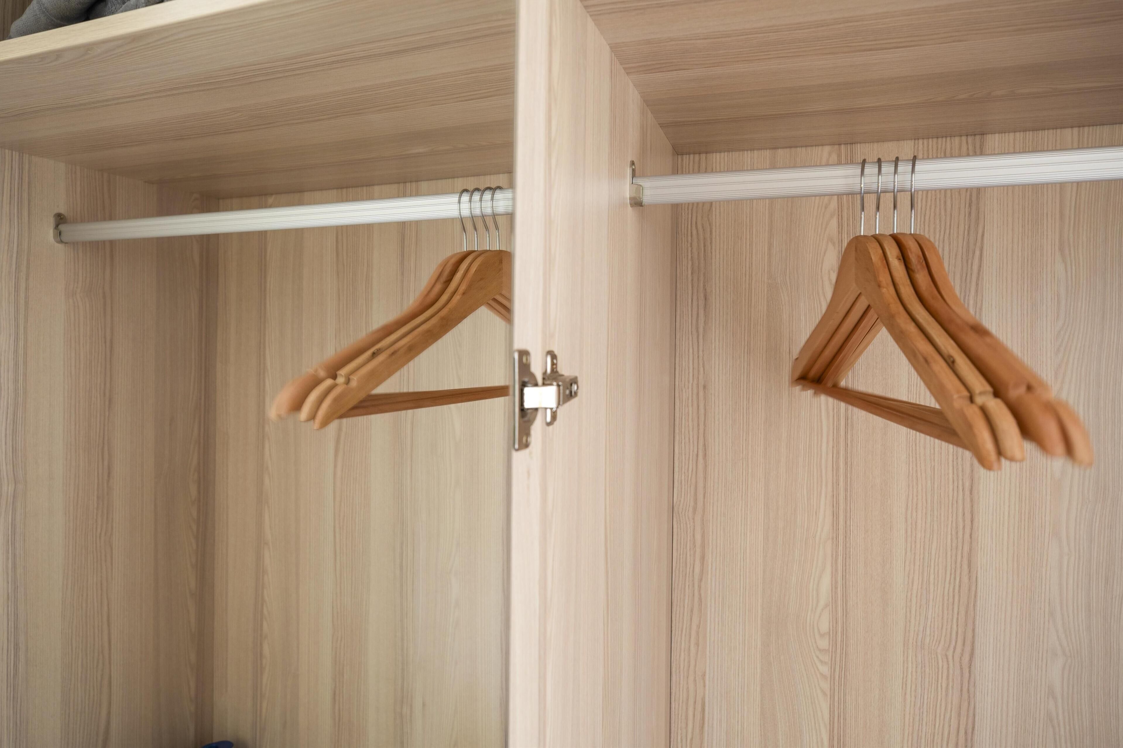 Un armario de madera con interior blanco y una barra metálica para colgar ropa.