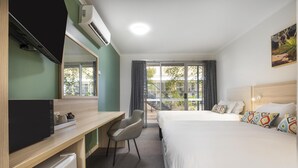 Una habitación de hotel con cama, escritorio, silla, televisor y ventana con cortinas.