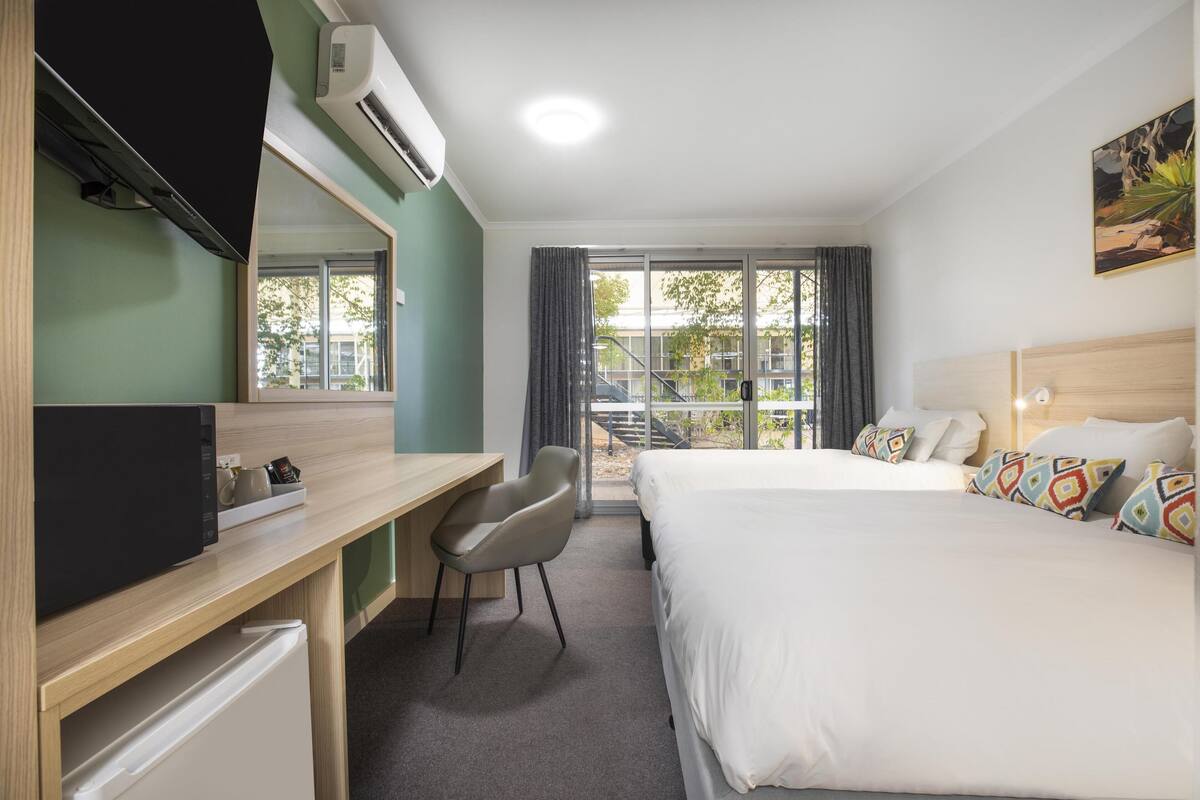 A hotel room with a bed, a desk, a chair, a TV, and a window with curtains.
