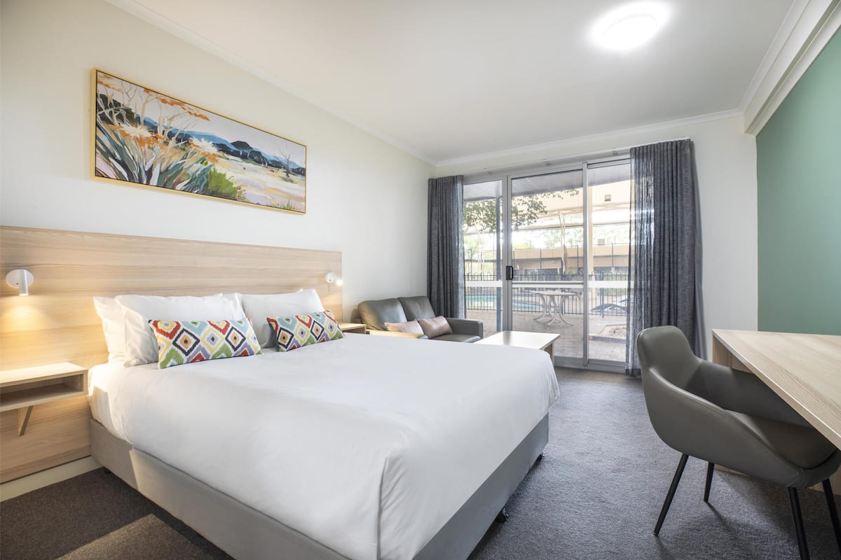 A hotel room with a large bed, a desk, a chair, a sofa, and a balcony with a view.