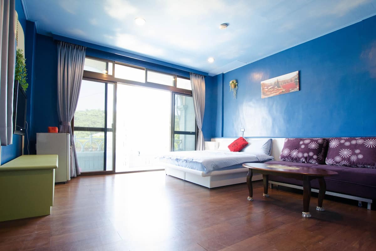 Une chambre moderne avec une grande fenêtre, un lit, un canapé et une petite table.