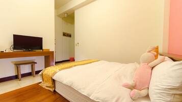 Un dormitorio con una cama, un escritorio con televisor, un pequeño banco y un peluche sobre la cama.