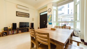 Une pièce spacieuse comprenant une grande table à manger en bois, plusieurs chaises, un téléviseur et une bibliothèque.