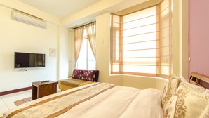 Une chambre d’hôtel avec un grand lit, un téléviseur fixé au mur et une fenêtre avec des rideaux.