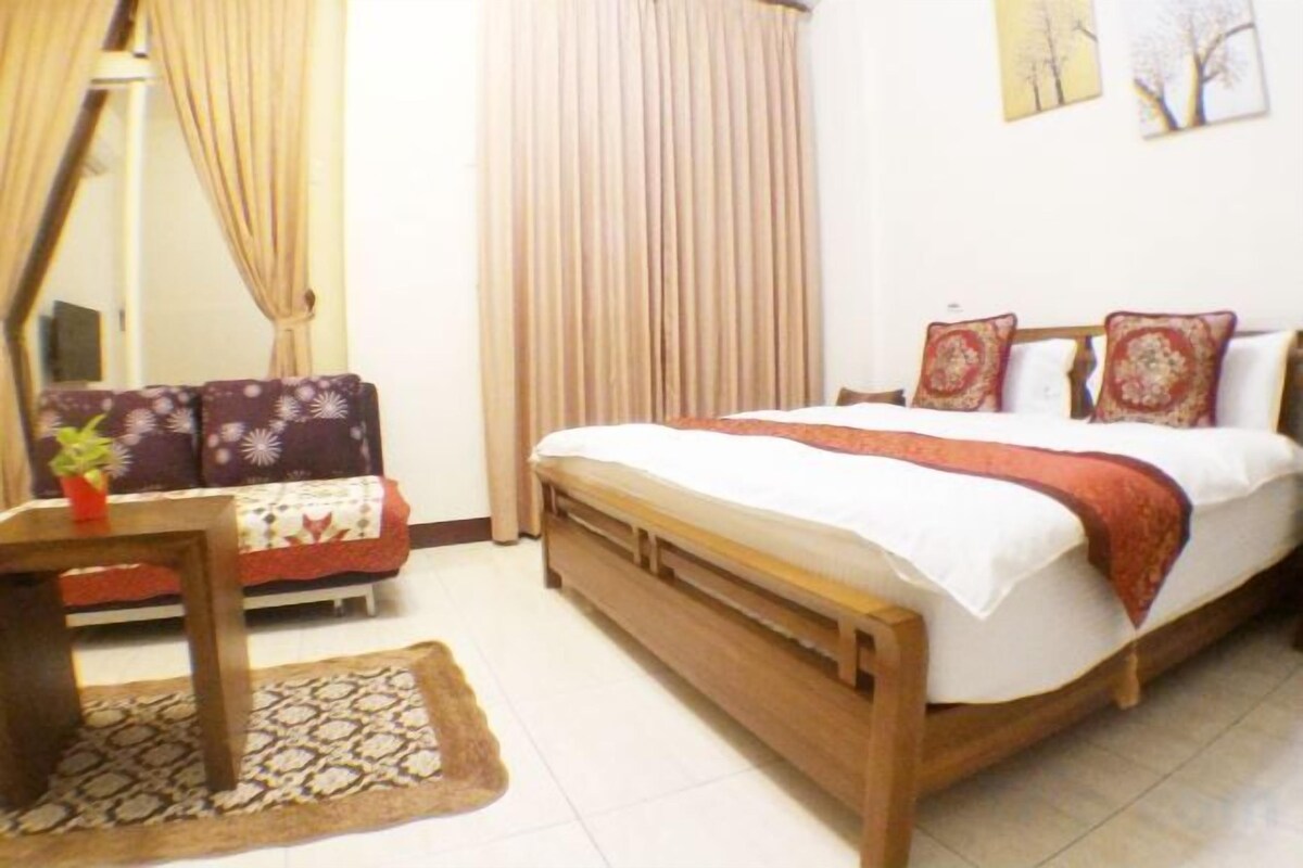 A bedroom with a bed, a sofa, a table, and curtains.
