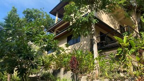 A two-story building with a balcony, surrounded by lush greenery and tropical plants.