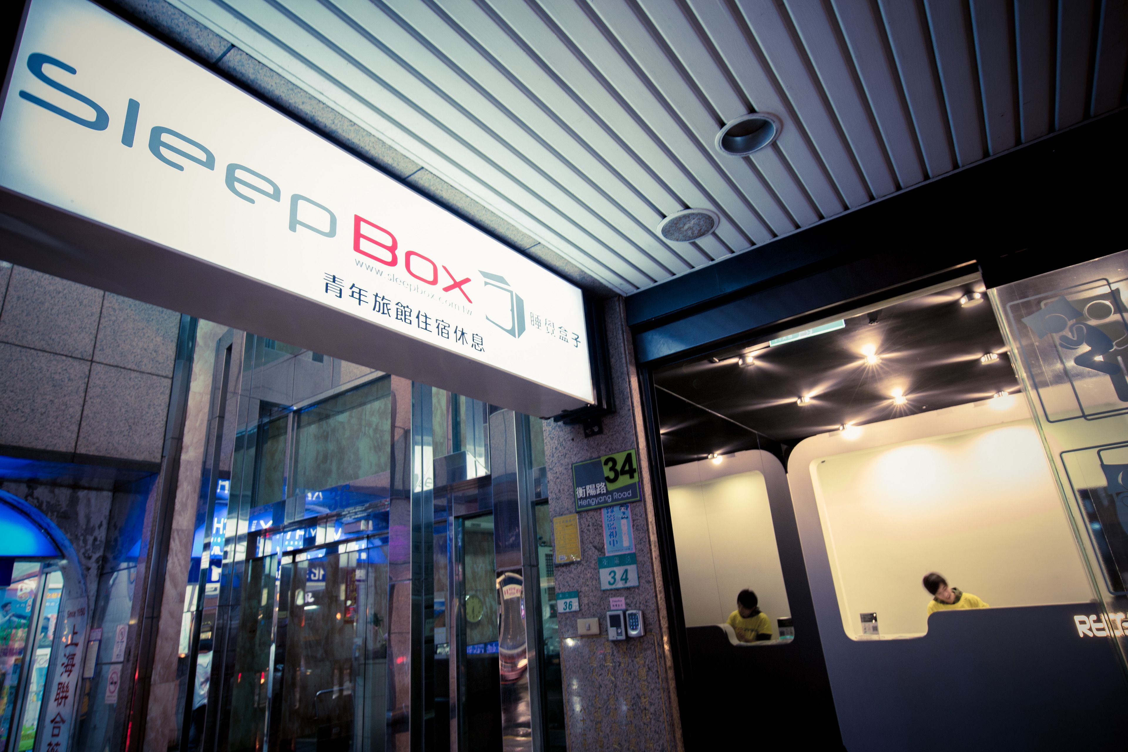 A SleepBox hotel entrance with a modern design, glass doors, and a sign indicating room number 34.