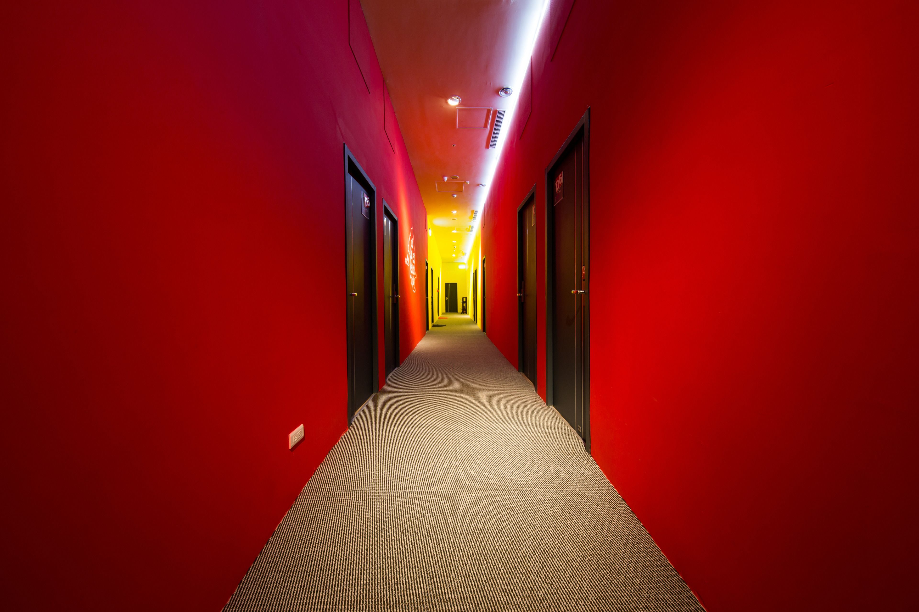 A corridor with red walls and a patterned carpet, leading to a door at the end.