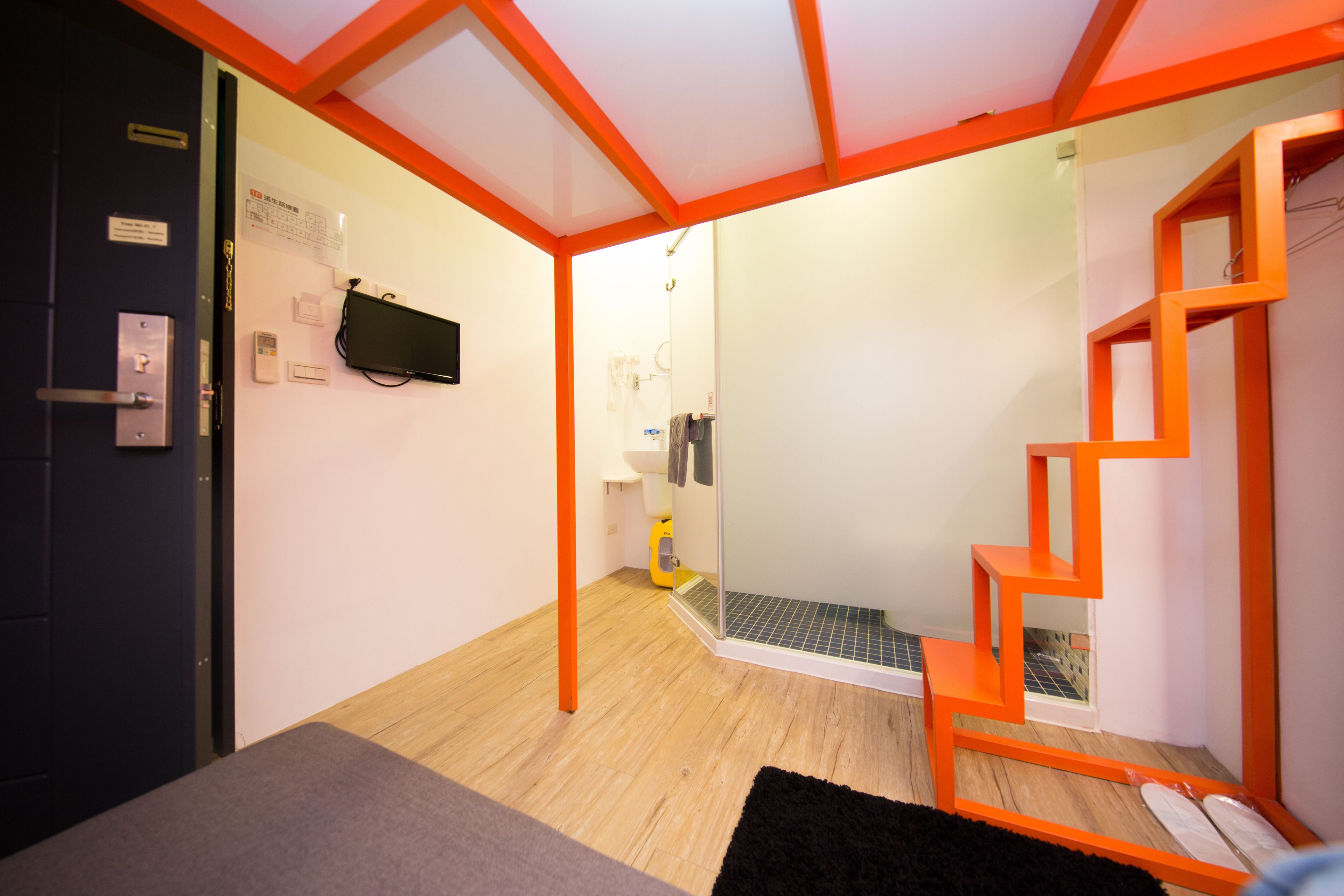 A compact room with a bed, a desk, a chair, a small bathroom with a shower, and a staircase.