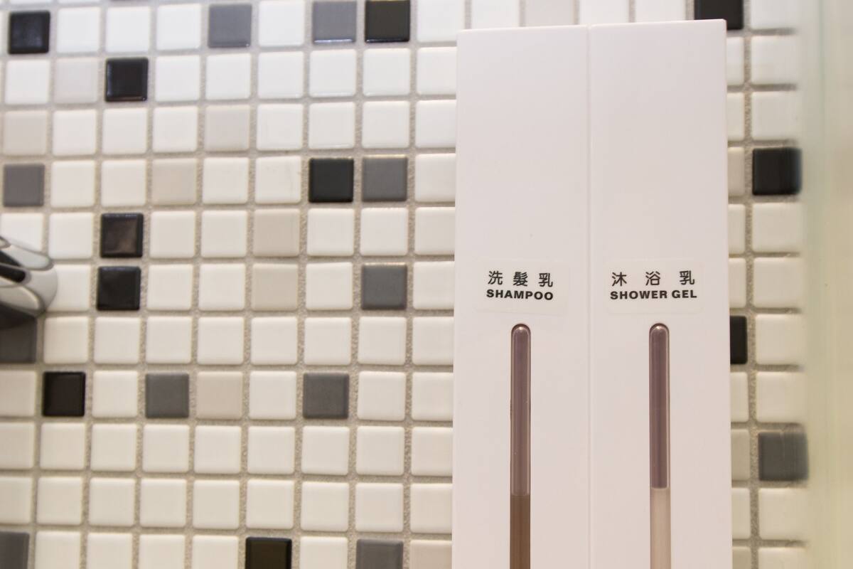 A bathroom with a tiled wall and a dispenser with two tubes labeled "shampoo" and "shower gel".