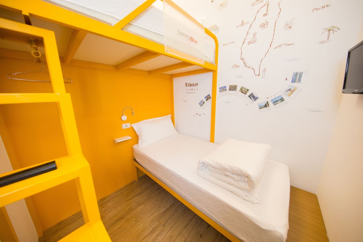 A single-bed room with a bunk bed, a map on the wall, and a television.