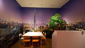 Un salón de conferencias con un mural de paisaje urbano, una mesa blanca y sillas anaranjadas.