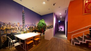 Una habitación con un mural de paisaje urbano, una mesa de comedor con sillas, una escalera y una recepción.