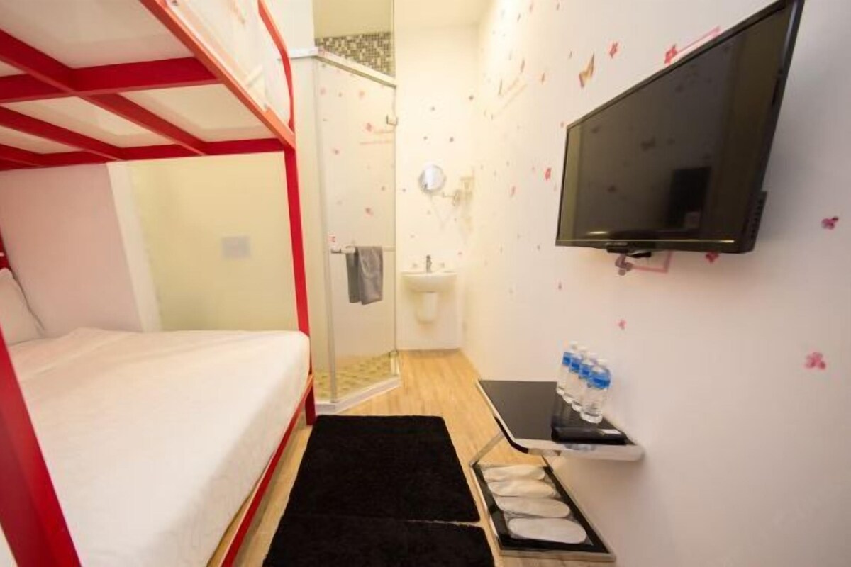A room with a bunk bed, a television mounted on the wall, a small sink, and a water bottle on a shelf.