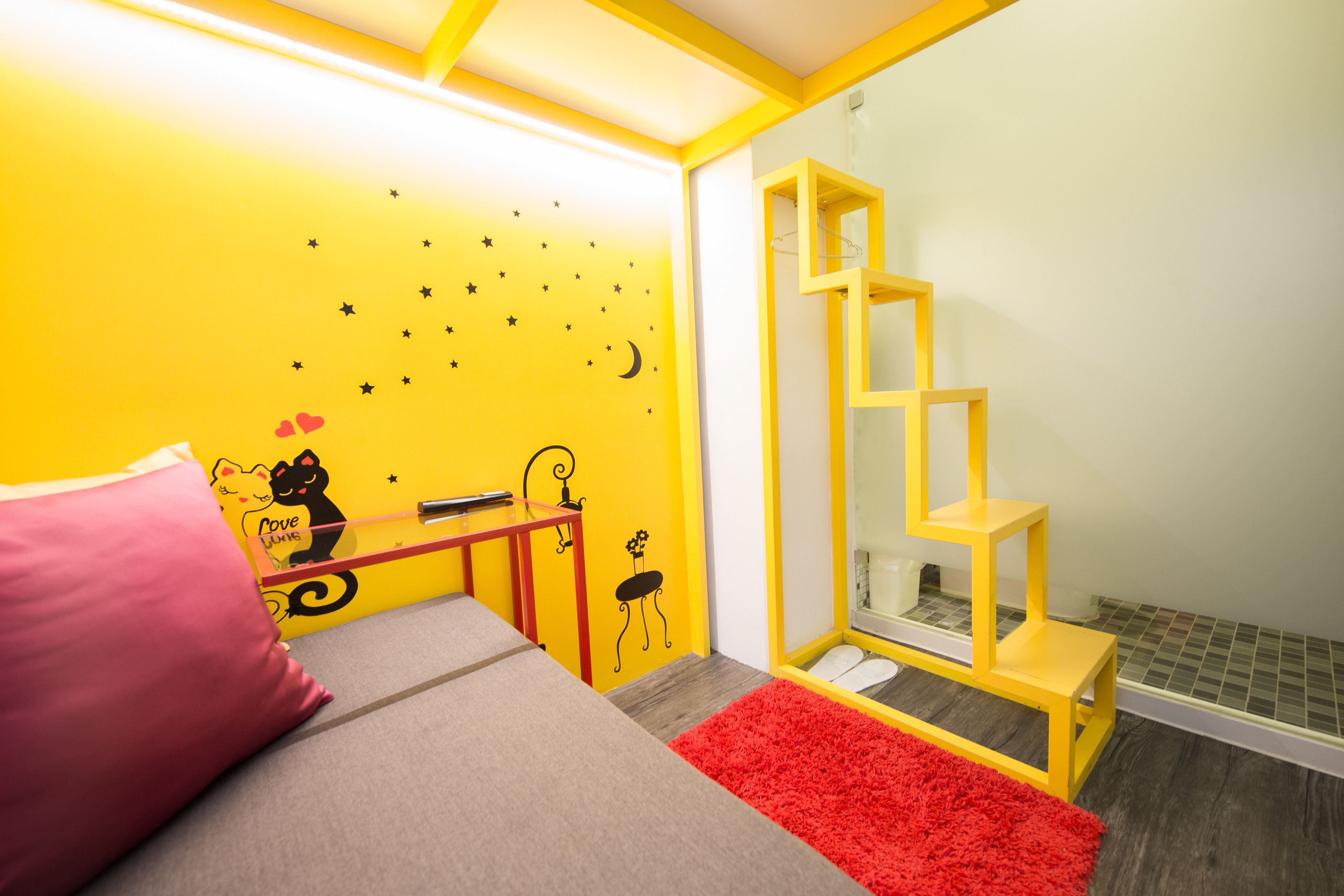 A child's bedroom with a bed, a red rug, a yellow wall with star decorations, and a small yellow shelf.