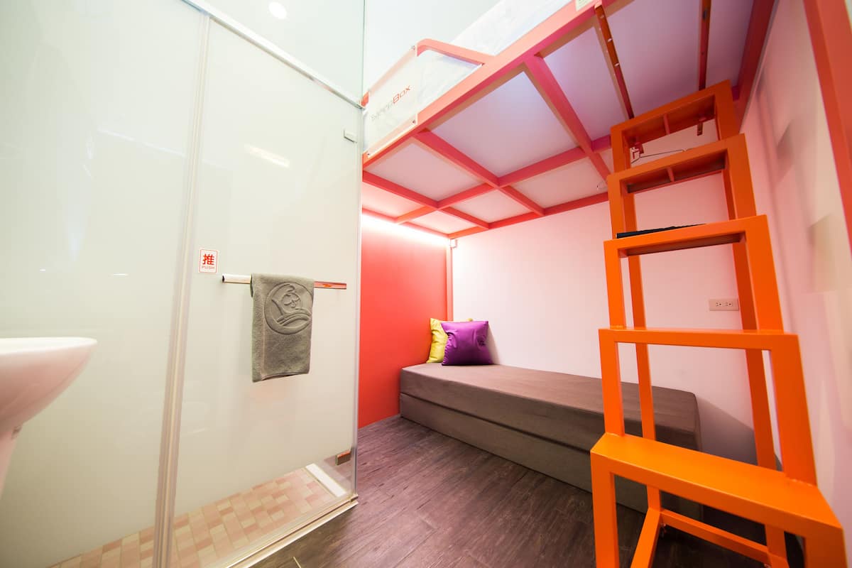 A compact room with a bed, a small seating area, and a shower.