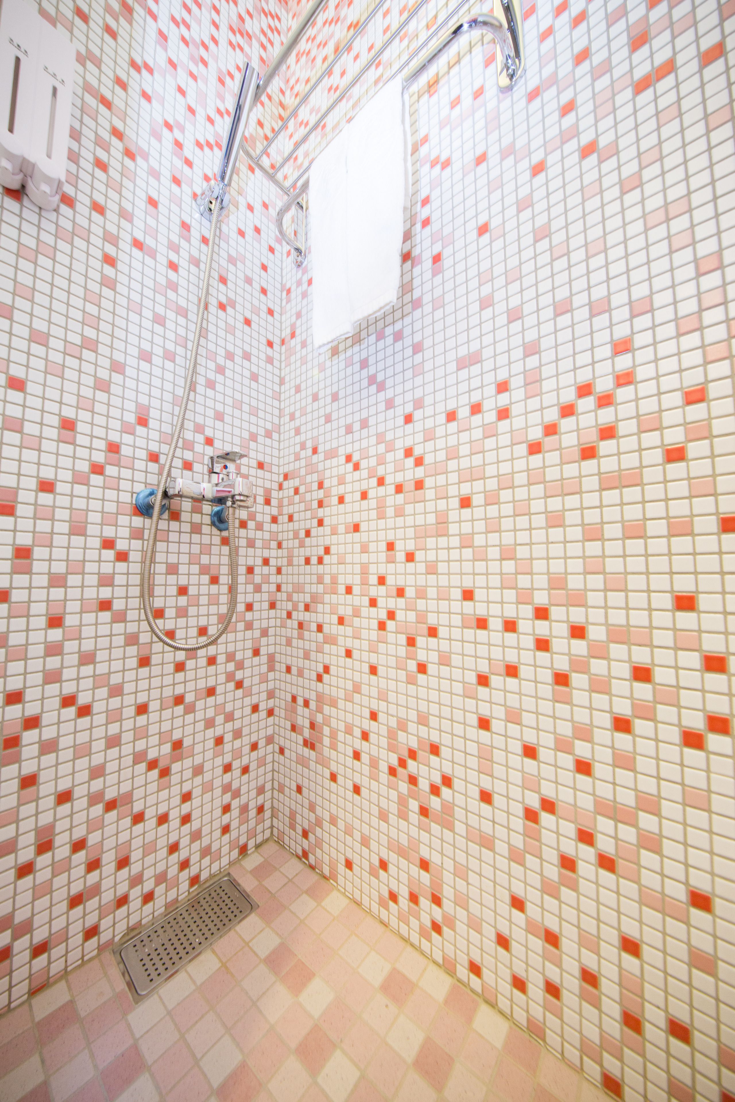 Een badkamer met een douche, betegelde wanden en een afvoer.