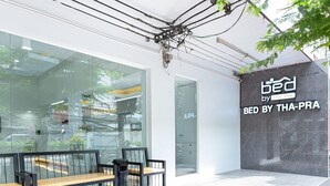 A modern storefront with a glass facade, a bench outside, and a sign reading "BED BY THA-PRA". - Bed by Tha-Pra Hotel and Apartment (Bangkok)