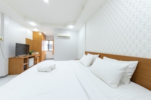 A hotel room with a neatly made bed, a television on a wooden stand, and a wall-mounted air conditioner. - Bed by Tha-Pra Hotel and Apartment (Bangkok)