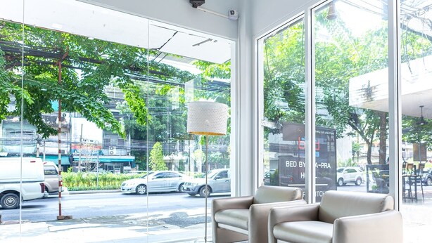 A modern interior with large windows, a sofa, and a hanging lamp. - Bed by Tha-Pra Hotel and Apartment (Bangkok)
