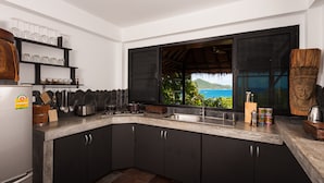 A modern kitchen with dark cabinets, a marble countertop, and a view of the ocean. - Koh Tao Heights Boutique Villas (Koh Tao)