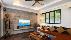A modern living room with a large flat-screen TV, a wooden coffee table, a sofa, and a decorative Buddha statue. - Koh Tao Heights Boutique Villas (Koh Tao)