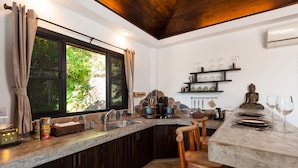 A kitchen with a marble countertop, wooden cabinets, a sink, and a window with curtains. - Koh Tao Heights Pool Villas (Koh Tao)