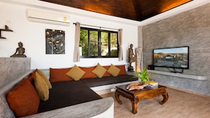 A modern living room with a sofa, a wooden coffee table, and a TV mounted on the wall. - Koh Tao Heights Pool Villas (Koh Tao)