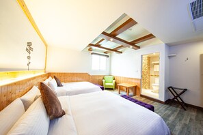 A hotel room with two beds, a green chair, a small table, and a bathroom visible through an open door.