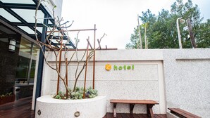 A hotel exterior with a wooden deck, a planter with trees, a bench, and a sign with a hotel logo. - Penghu Royal (Magong)