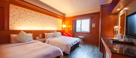 Ein Hotelzimmer mit zwei Betten, einem kleinen Tisch, einem Fernseher und einem Fenster.
