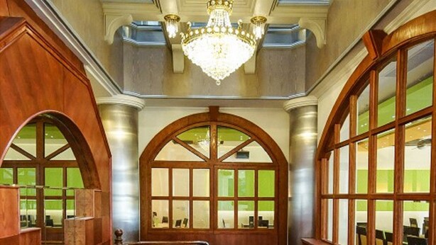 A grand staircase with wooden railings and a chandelier, leading to a room with large arched windows and a green-tinted glass wall. - Penghu Royal (Magong)