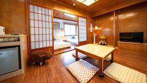 A traditional Japanese-style room with tatami flooring, a low table, a television, and a small refrigerator. - Penghu Royal (Magong)